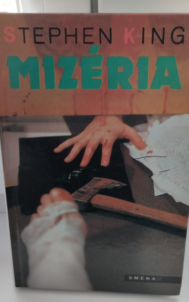 Obálka knihy, na ktorej je noha v sadre, ruka a sekera. Nad tým nápis Mizéria.